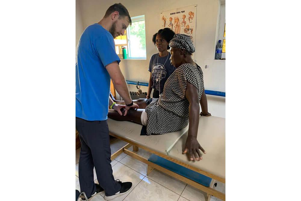 Male physical therapy professor examines female Haitian patient's leg