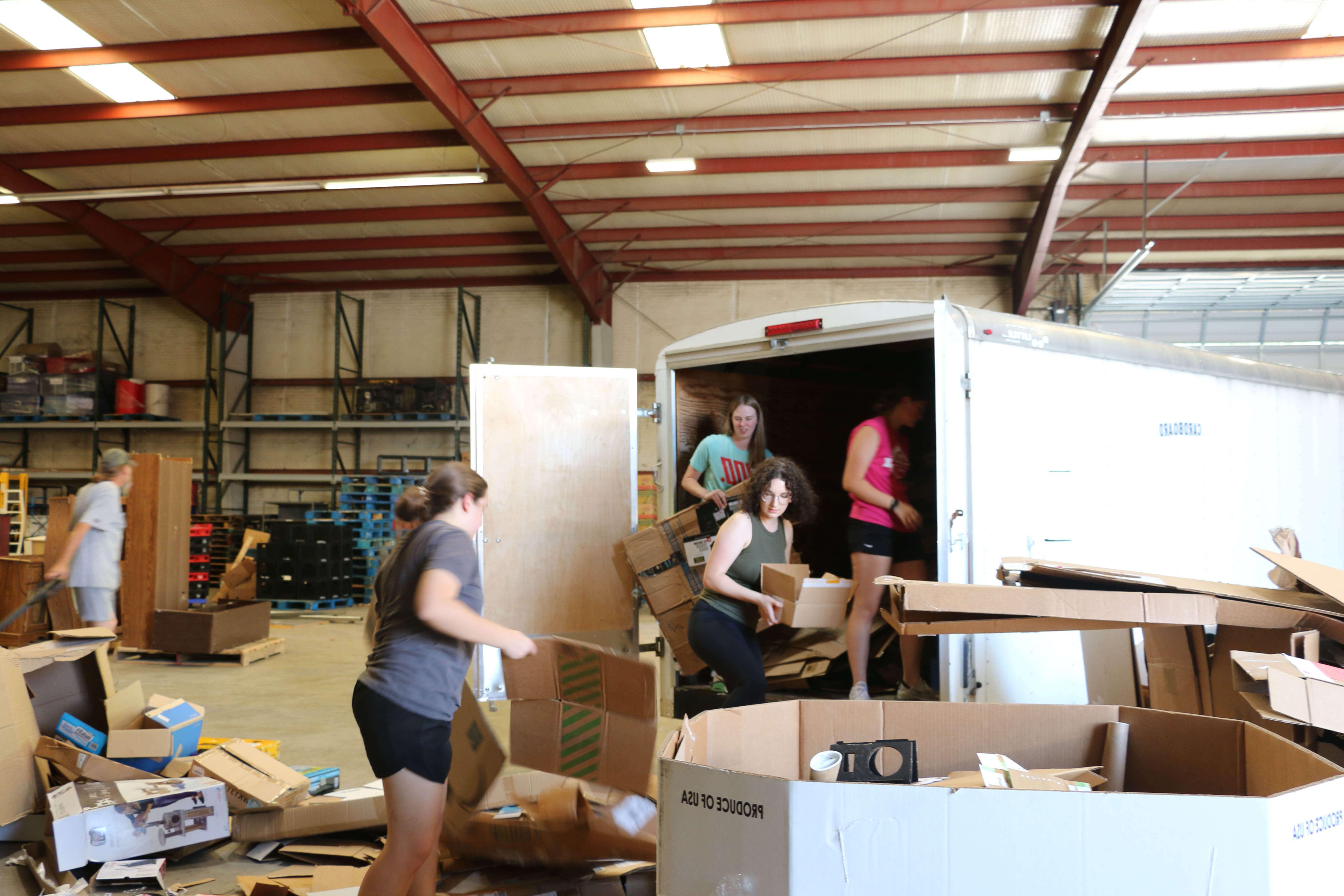 students serve in ministry warehouse unloading cardboard from trailer to recycle