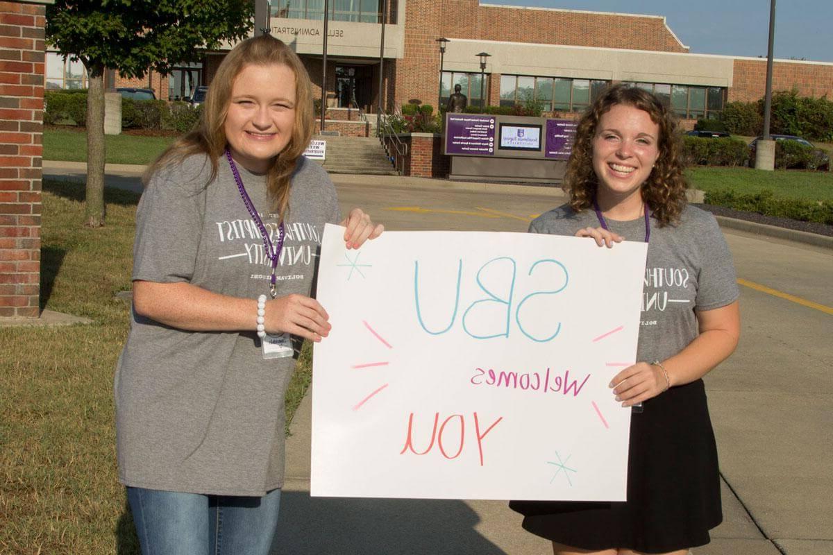 Two college girls hold poster board sign that says SBU welcomes you