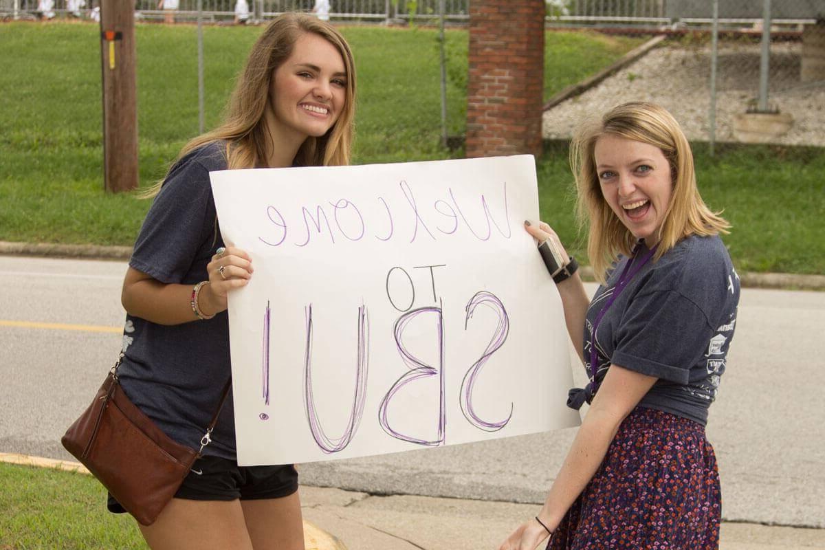 Two female students hold poster board sign that says Welcome to SBU