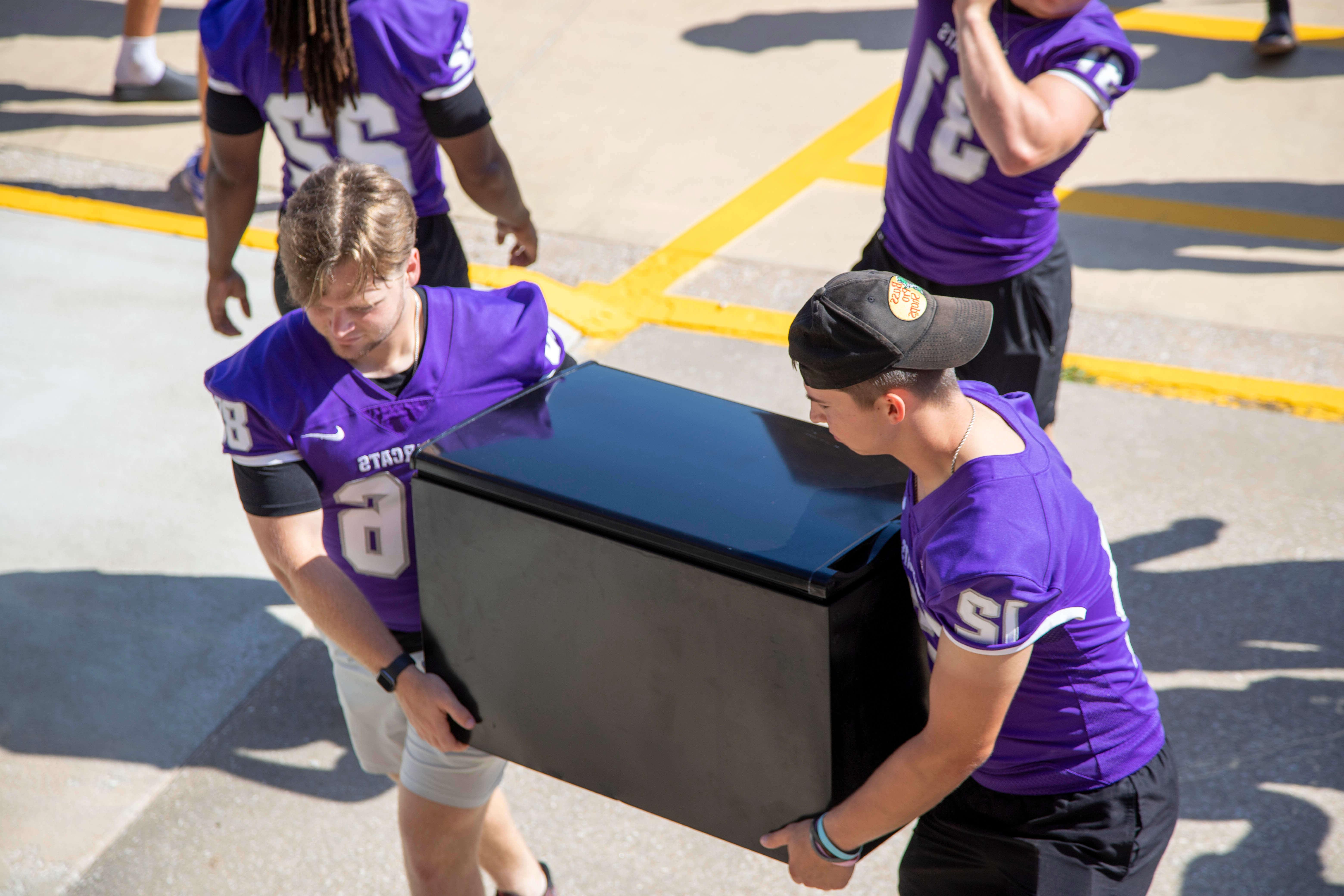 football players help carry furniture into dorm