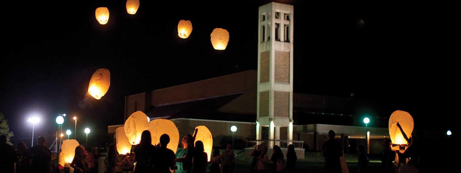 学生s release lanterns into night sky in front of bell tower